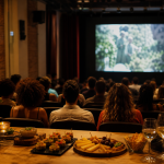Público acompanha sessão de cinema cultural com mesa de degustação em primeiro plano