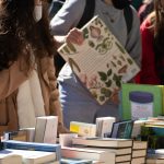 Pessoas observam livros em uma feira literária ao ar livre, em um dia ensolarado.