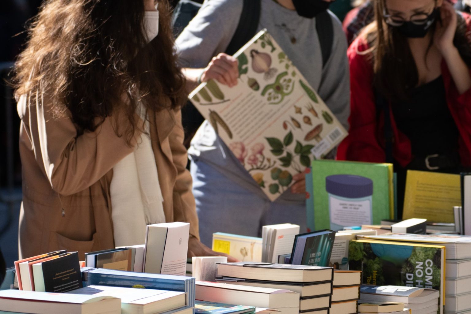 Pessoas observam livros em uma feira literária ao ar livre, em um dia ensolarado.