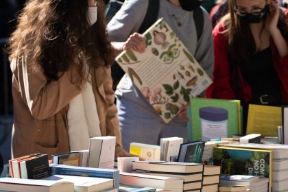 Pessoas observam livros em uma feira literária ao ar livre, em um dia ensolarado.
