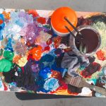 Paleta de artista com tintas de várias cores e pincéis, representando o processo de criação artística