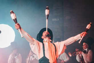 Artista circense equilibra e lança claves durante uma apresentação teatral.