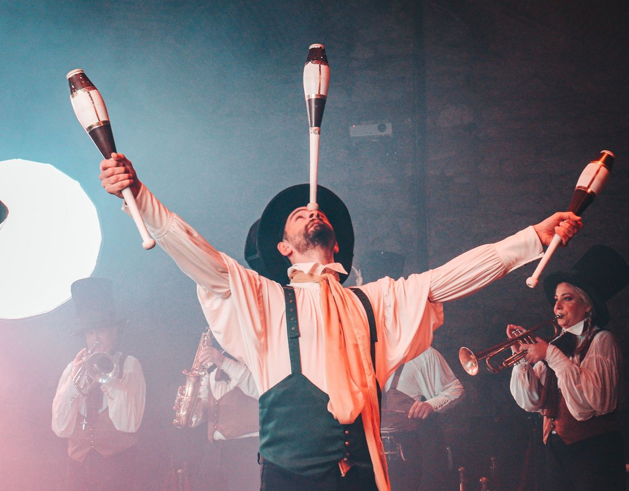 Artista circense equilibra e lança claves durante uma apresentação teatral.