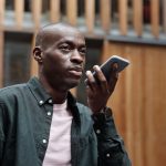 Homem usa comandos de voz no smartphone em um ambiente urbano.