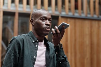 Homem usa comandos de voz no smartphone em um ambiente urbano.