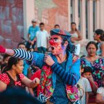 Artista caracterizado de palhaço se apresenta na rua diante de um público diverso.