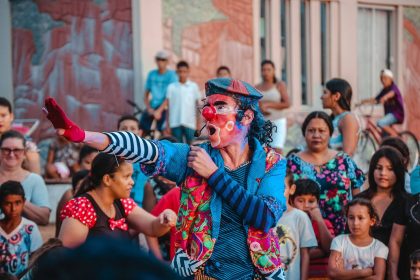 Artista caracterizado de palhaço se apresenta na rua diante de um público diverso.