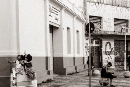 Artistas fantasiados riem juntos em uma esquina de rua calçada.