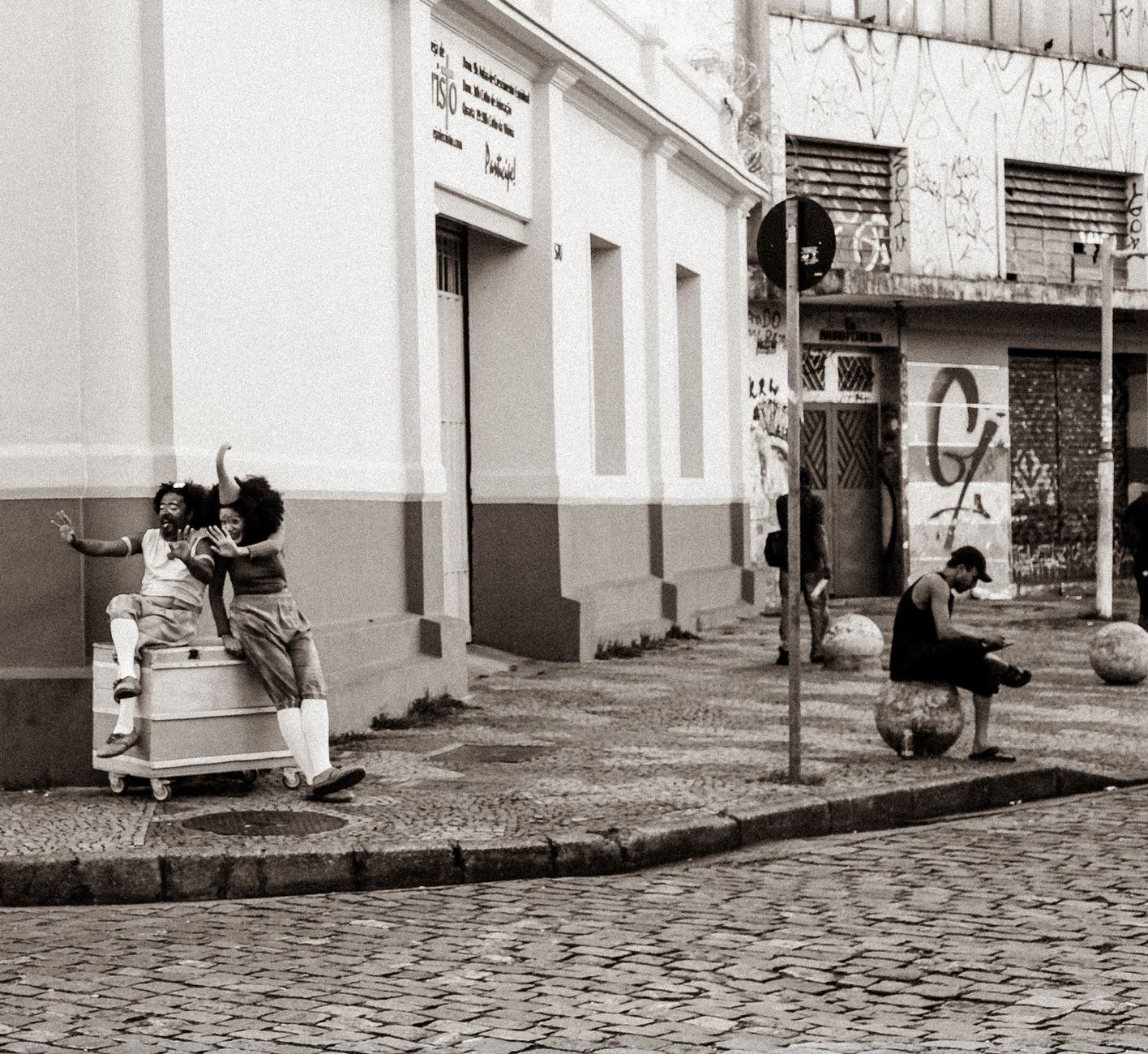 Artistas fantasiados riem juntos em uma esquina de rua calçada.